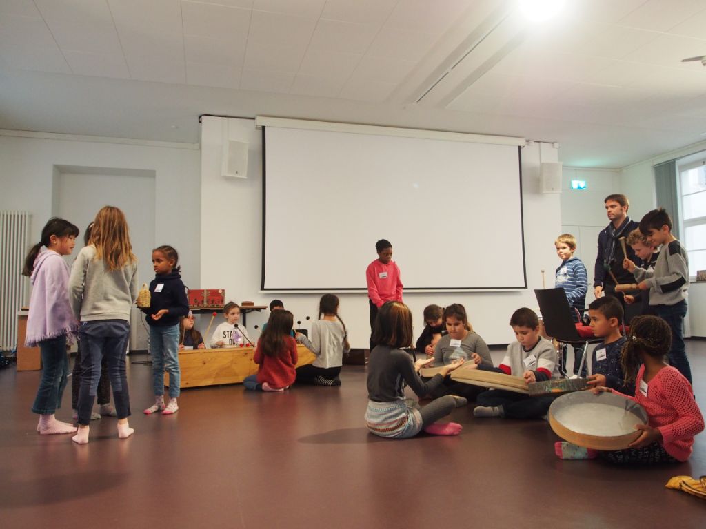 Die Kinder stehen oder sitzen an Perkussionsinstrumenten und spielen die einstudierten Klänge.
